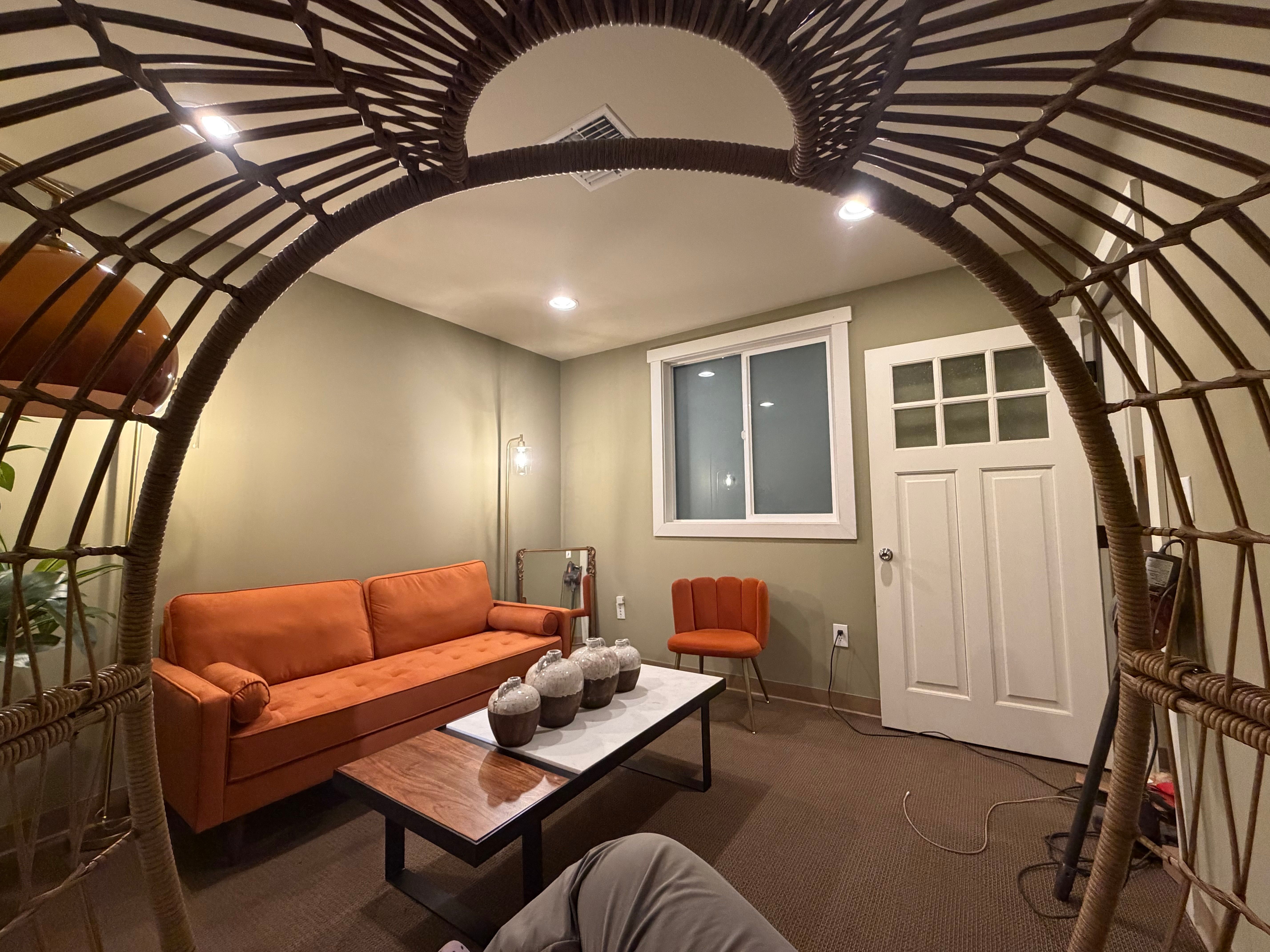 View of the orange sofa and seating framed through the hanging wicker chair